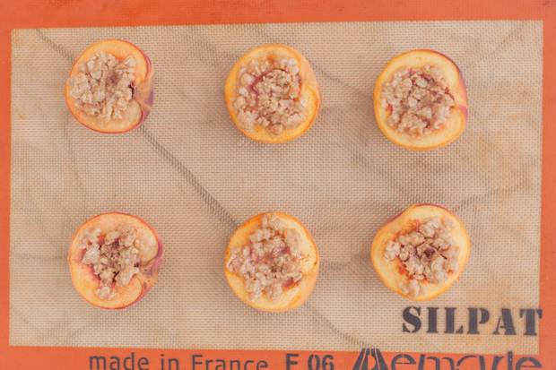 Halved peaches topped with crisp topping on a baking tray with silpat.